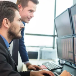 Two men reviewing financial data on multiple monitors.